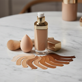 Luxury foundation bottle with pump dispenser alongside beauty blender and brush with diverse skin tone shade swatches on white marble