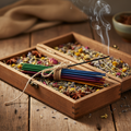 Bundle of colorful premium incense sticks tied with twine with one lit stick releasing smoke surrounded by dried herbs and flowers
