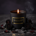 Dramatic dark luxury scented candle in matte black jar with gold label surrounded by dark dried roses and black crystals