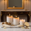 Three luxury scented candles in frosted glass jars with gold lids glowing warmly on marble surface with dried botanicals